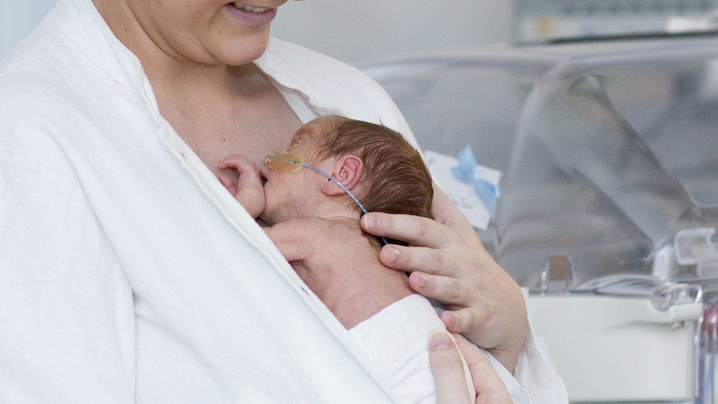 Kvinde med lille nyfødt hud mod hud - kuvøse i baggrunden