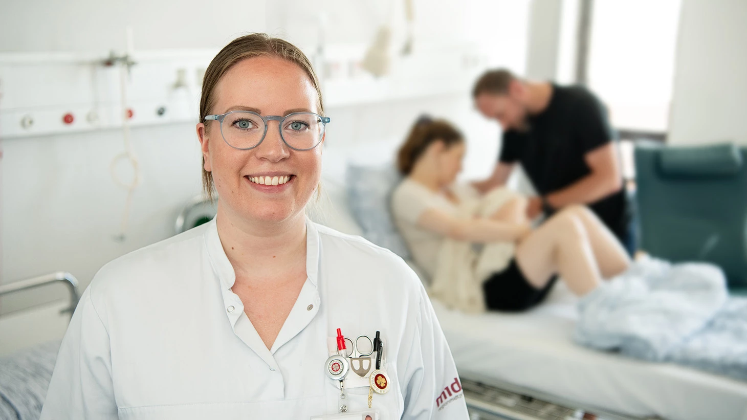 Sygeplejerske på sengestue med barselsfamilie i baggrunden